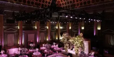 Interior view of a grand ballroom with a stained glass ceiling, marble columns, and round tables set for a formal event.