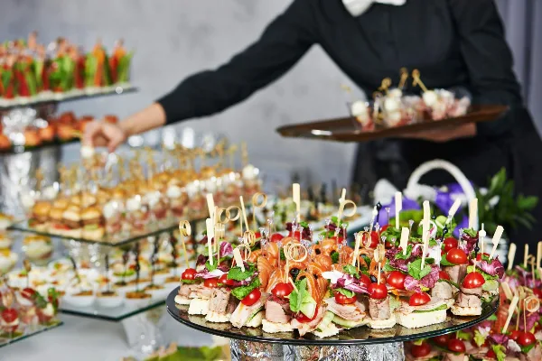 A catering server in black attire presents a tray of gourmet appetizers and canapés at an event.