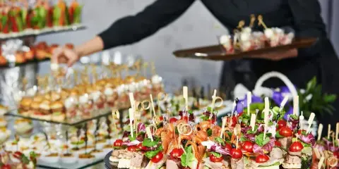 A catering server in black attire presents a tray of gourmet appetizers and canapés at an event.