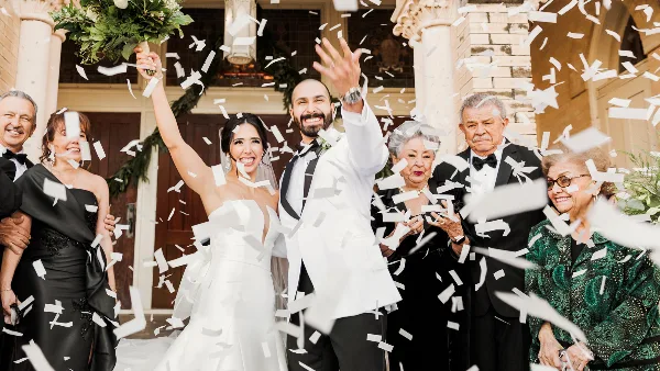 A bride and groom celebrating with confetti and family members at a wedding venue.