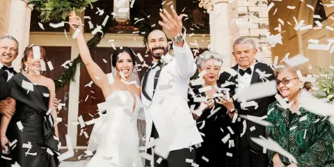 A bride and groom celebrating with confetti and family members at a wedding venue.
