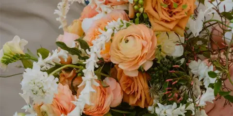 Close-up of a hand-held wedding bouquet featuring peach roses, ranunculus, and white flowers