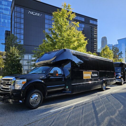 A black Cooper Global luxury shuttle bus parked on a city street.