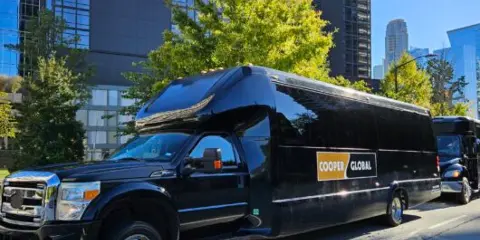 A black Cooper Global luxury shuttle bus parked on a city street.