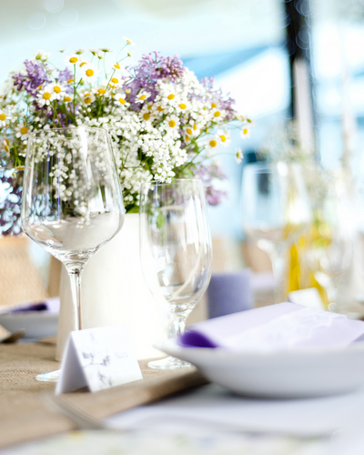 A floral centerpiece featuring white and purple flowers on a decorated event table with glassware.