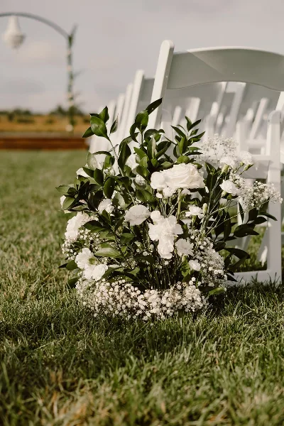 White wedding chairs and floral arrangements set up on a grassy lawn.