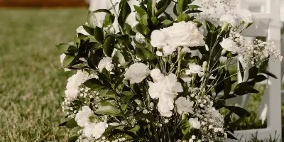 White wedding chairs and floral arrangements set up on a grassy lawn.