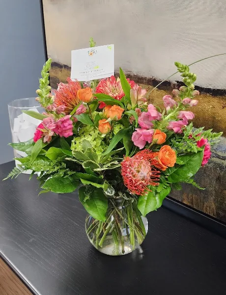 A colorful floral arrangement in a glass vase with a Flower Mill card inserted.