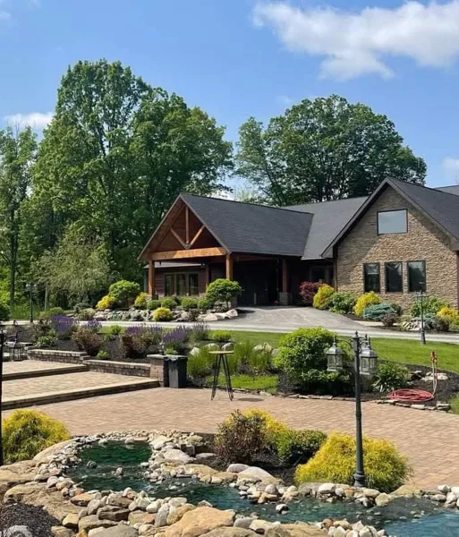 Exterior view of Stone Creek Lodge venue building with stone facade, wooden entry, landscaped gardens, and a small water feature in the foreground.