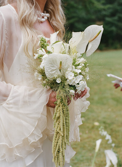 A bride holding a white and green modern wedding bouquet with anthuriums and amaranthus.