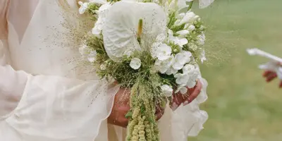 A bride holding a white and green modern wedding bouquet with anthuriums and amaranthus.