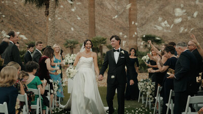 Bride and groom walking down the aisle at a wedding ceremony with guests seated on either side.