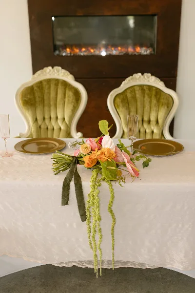 A floral wedding centerpiece featuring pink and orange blooms and trailing greenery on a white tablecloth.