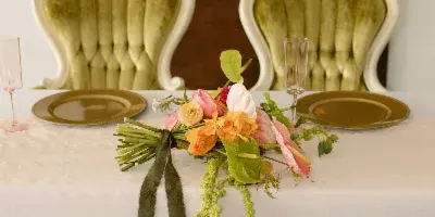 A floral wedding centerpiece featuring pink and orange blooms and trailing greenery on a white tablecloth.