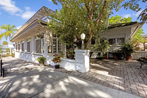 Exterior view of the Pisces Rising restaurant, a white historic bungalow with a paved patio and lush landscaping.