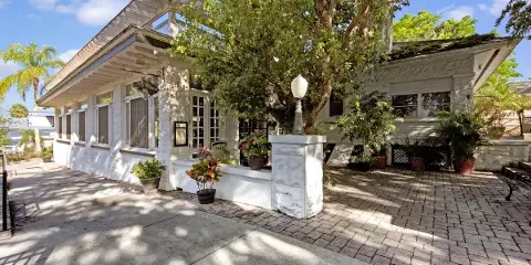 Exterior view of the Pisces Rising restaurant, a white historic bungalow with a paved patio and lush landscaping.