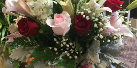 A floral arrangement with red and pink roses, white lilies, and baby's breath tied with a ribbon, displayed in a florist shop.