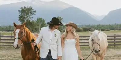 A bride and groom walking with two horses in a Montana field with mountains in the background.