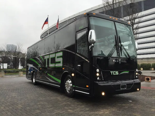 A black TCS charter bus parked on a brick road.