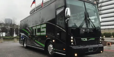 A black TCS charter bus parked on a brick road.