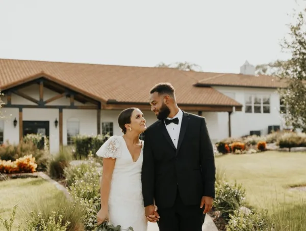 A bride and groom standing in the manicured gardens in front of the Sterling Event Venue's Tuscan-style building.