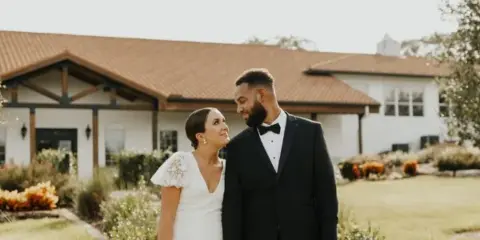 A bride and groom standing in the manicured gardens in front of the Sterling Event Venue's Tuscan-style building.