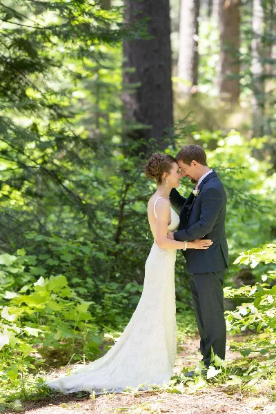 A bride and groom embracing in a lush, green forest setting.