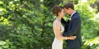 A bride and groom embracing in a lush, green forest setting.