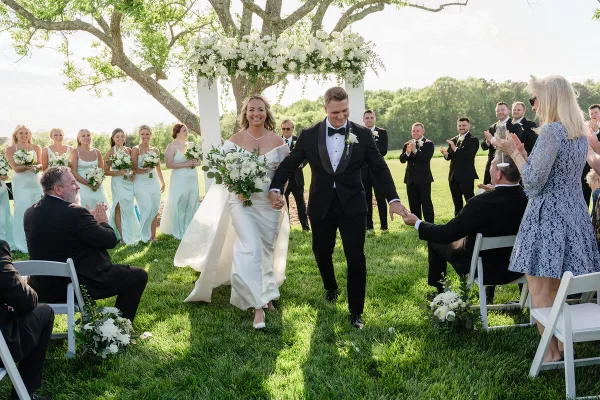 A bride and groom walking down the aisle after their wedding ceremony, surrounded by their wedding party and guests.