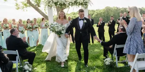 A bride and groom walking down the aisle after their wedding ceremony, surrounded by their wedding party and guests.