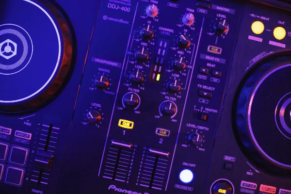 Close-up of a Pioneer DJ controller with glowing blue and purple lighting, showing knobs, faders, and cue buttons.