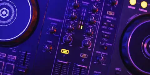 Close-up of a Pioneer DJ controller with glowing blue and purple lighting, showing knobs, faders, and cue buttons.