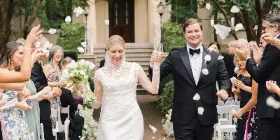 A bride and groom walking down a brick aisle lined with white flowers and guests during a wedding ceremony.