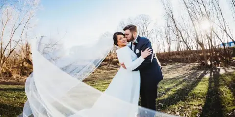 A bride and groom embracing outdoors with the bride's veil flowing in the wind.