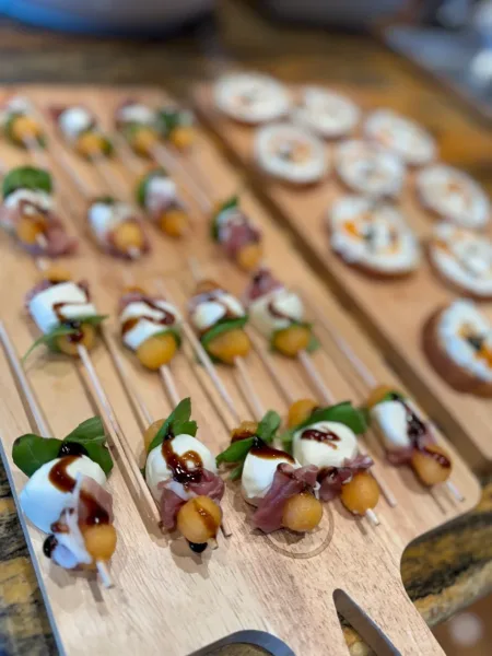 A wooden serving board filled with catering appetizers including mozzarella and prosciutto skewers and bruschetta.