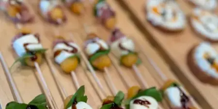 A wooden serving board filled with catering appetizers including mozzarella and prosciutto skewers and bruschetta.