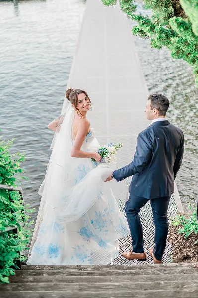 A bride and groom standing on a wooden pier by the water, with the bride looking back at the camera.