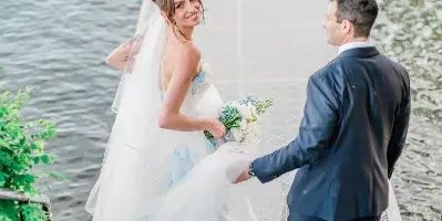 A bride and groom standing on a wooden pier by the water, with the bride looking back at the camera.