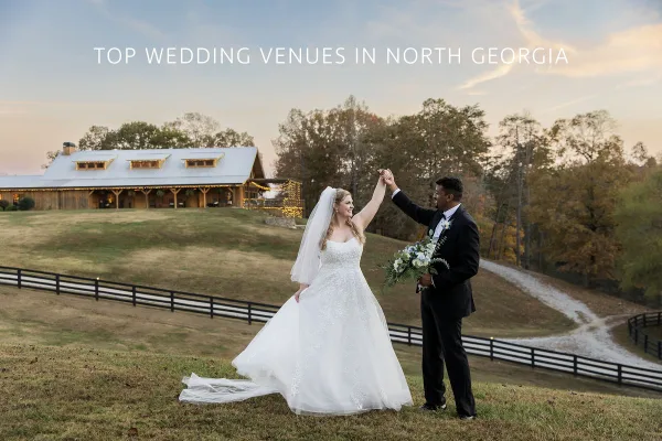 A bride and groom dancing outdoors in front of a rustic wooden barn venue during the golden hour.