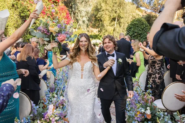 A bride and groom walking down a floral-decorated aisle at an outdoor wedding.