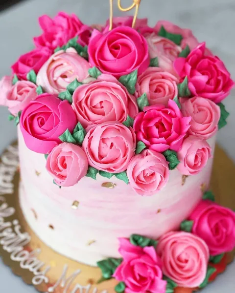 A close-up of a white cake decorated with elaborate pink and magenta buttercream roses and green leaves.