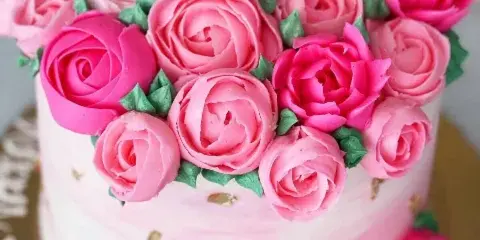 A close-up of a white cake decorated with elaborate pink and magenta buttercream roses and green leaves.