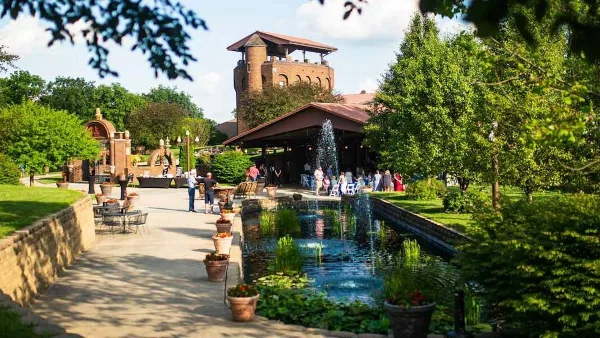 Exterior view of the Castle Unicorn wedding venue showing a brick tower, reception pavilion, and a central water feature with guests.