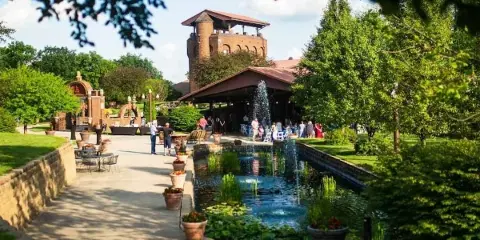 Exterior view of the Castle Unicorn wedding venue showing a brick tower, reception pavilion, and a central water feature with guests.