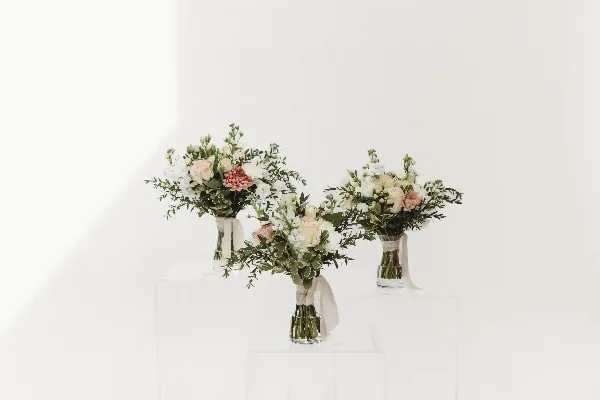 Three floral arrangements with white and pink flowers in clear vases on white pedestals.