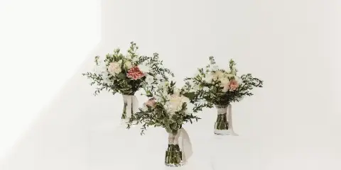 Three floral arrangements with white and pink flowers in clear vases on white pedestals.