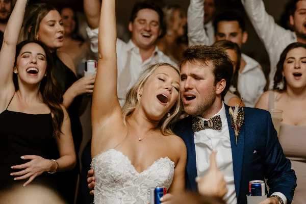 A bride and groom singing along with their guests on the dance floor at a wedding