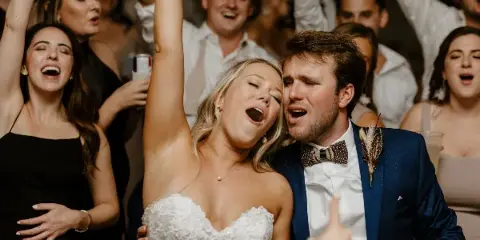 A bride and groom singing along with their guests on the dance floor at a wedding