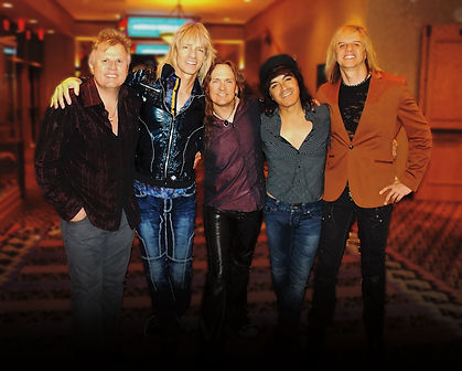 A group of five musicians standing together in a casual pose.