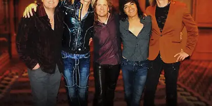 A group of five musicians standing together in a casual pose.